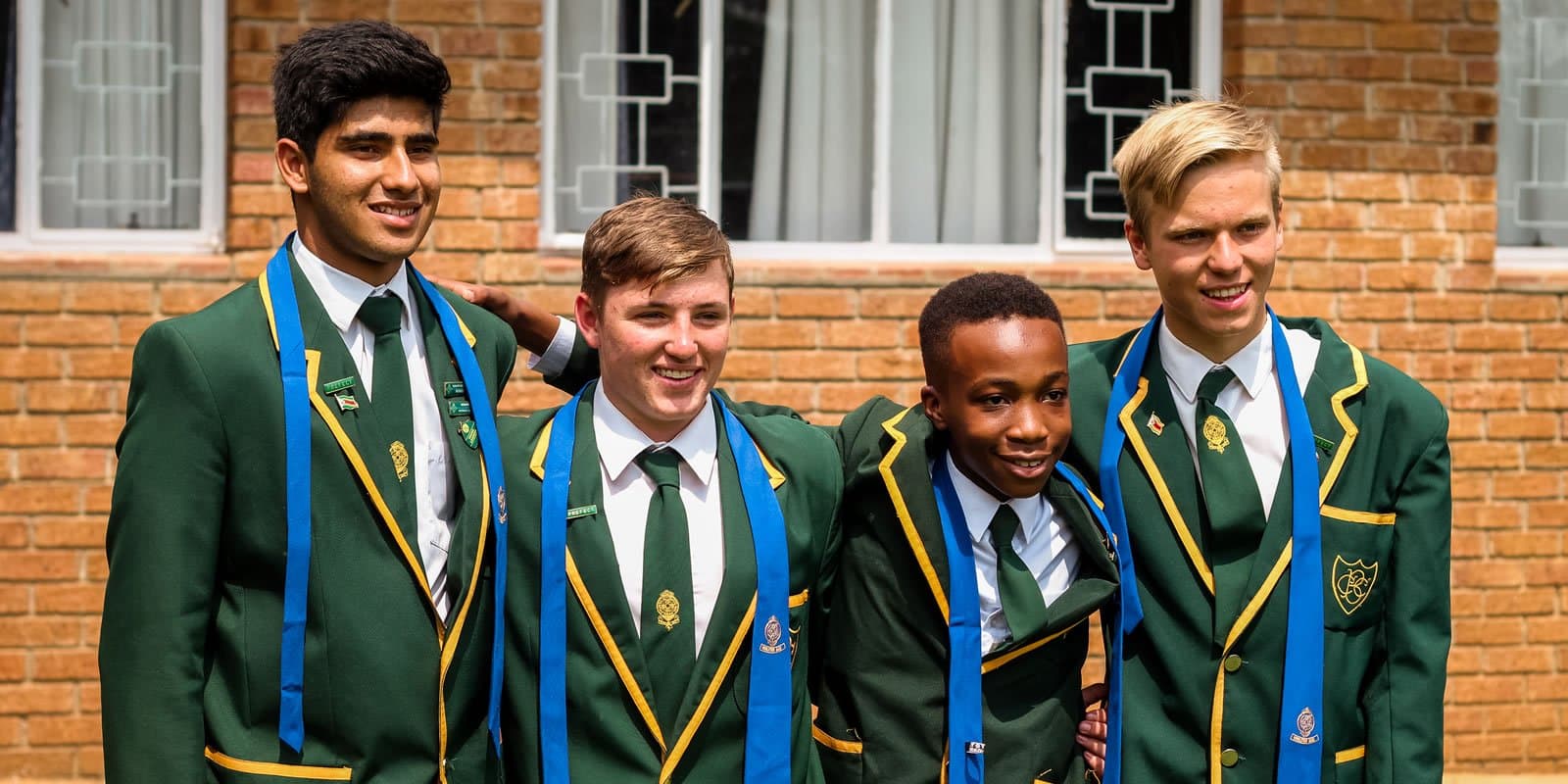 Four CBC boys in the College's green and gold blazers outside a red-brick school building